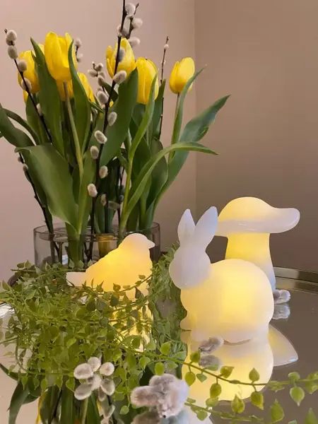 Vase med påskeblomster og tre lysfigurer ved siden av.