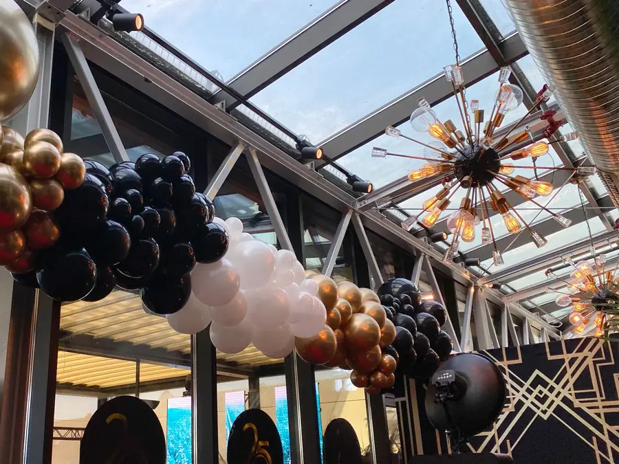 Ballonger i fargene gull, svart og hvit hengende foran flere store vinduer