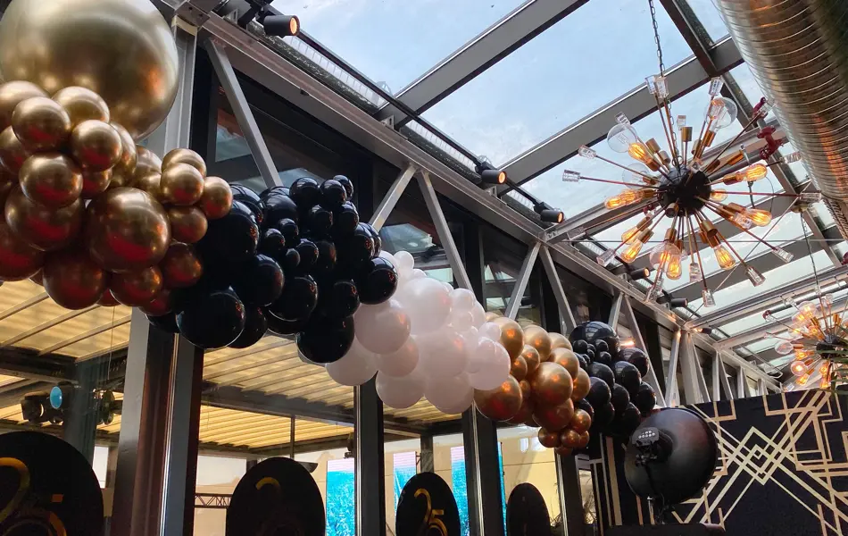 Ballonger i fargene gull, svart og hvit hengende foran flere store vinduer