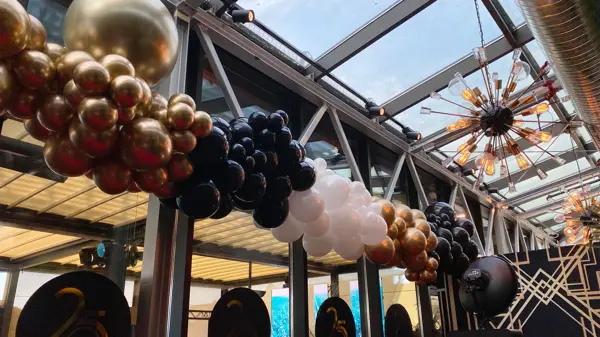 Ballonger i fargene gull, svart og hvit hengende foran flere store vinduer