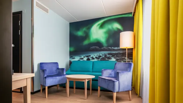 Junior suite med sittegruppe, lite rundt bord, gule gardiner og nordlys bilde på veggen i bakgrunnen
