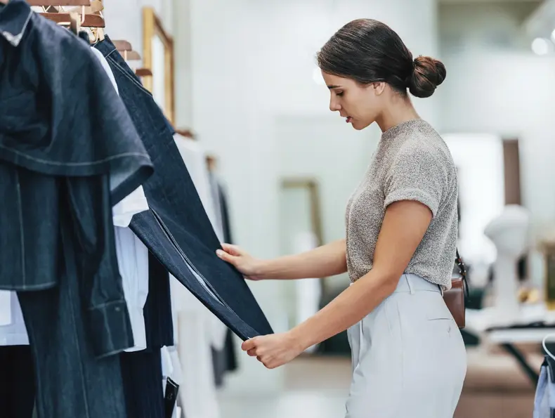Ung kvinne står i klesbutikk og ser på klær