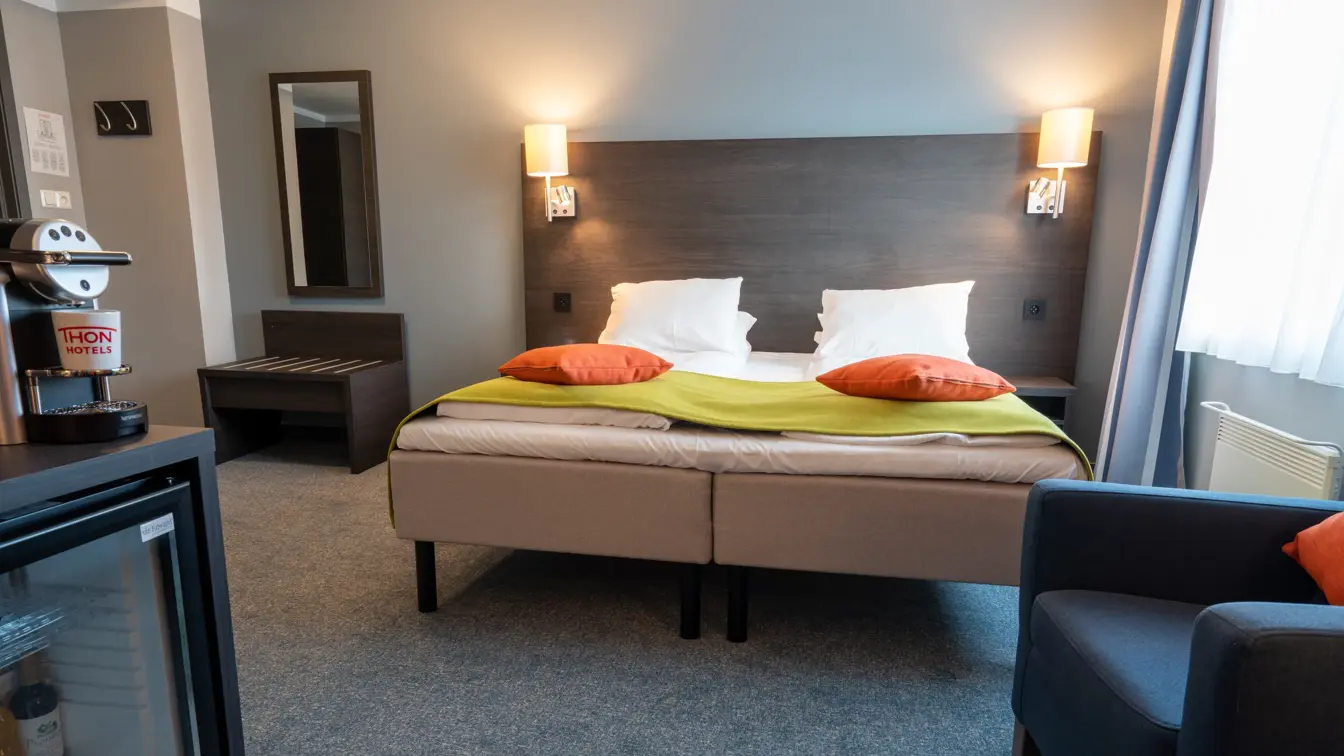 Dobbeltseng, vindu, blå lenestol, minibar, kaffemaskin