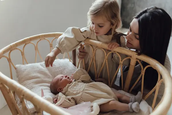 Nyfødt baby i krybbe av bambus, med mor og storesøster ved siden av