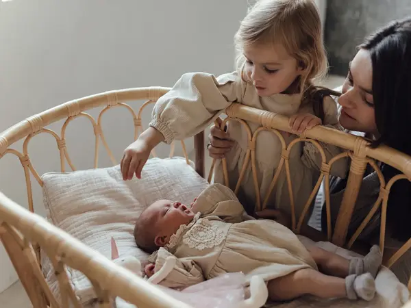 Nyfødt baby i krybbe av bambus, med mor og storesøster ved siden av