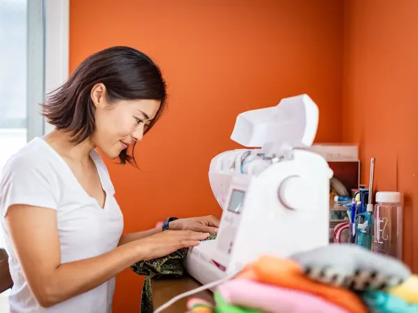 Young woman sewing clothes at home with orange wall in the background