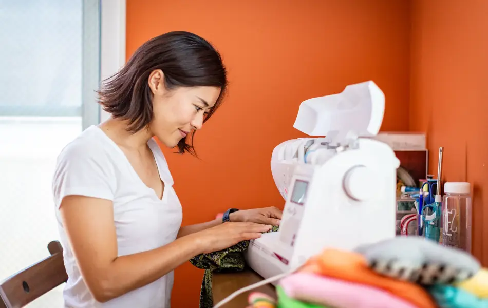 Young woman sewing clothes at home with orange wall in the background