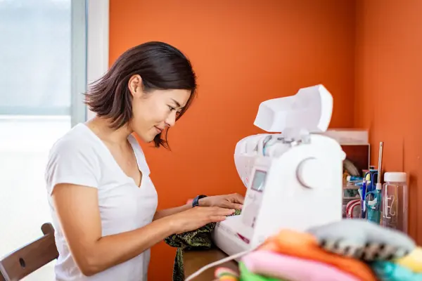 Young woman sewing clothes at home with orange wall in the background