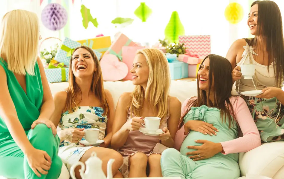 Group of female friends sitting on sofa, drinking tea on baby shower party, laughing.