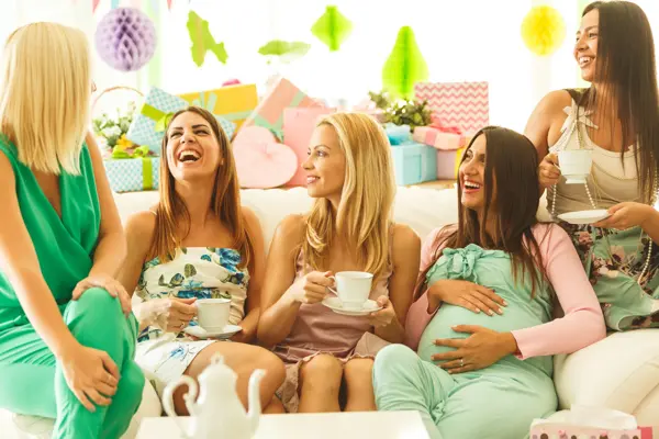 Group of female friends sitting on sofa, drinking tea on baby shower party, laughing.