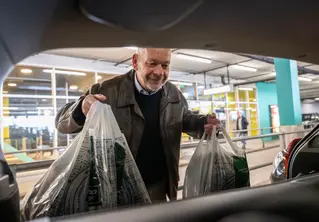 En mann som setter inn handleposer i bagasjerommet. 
