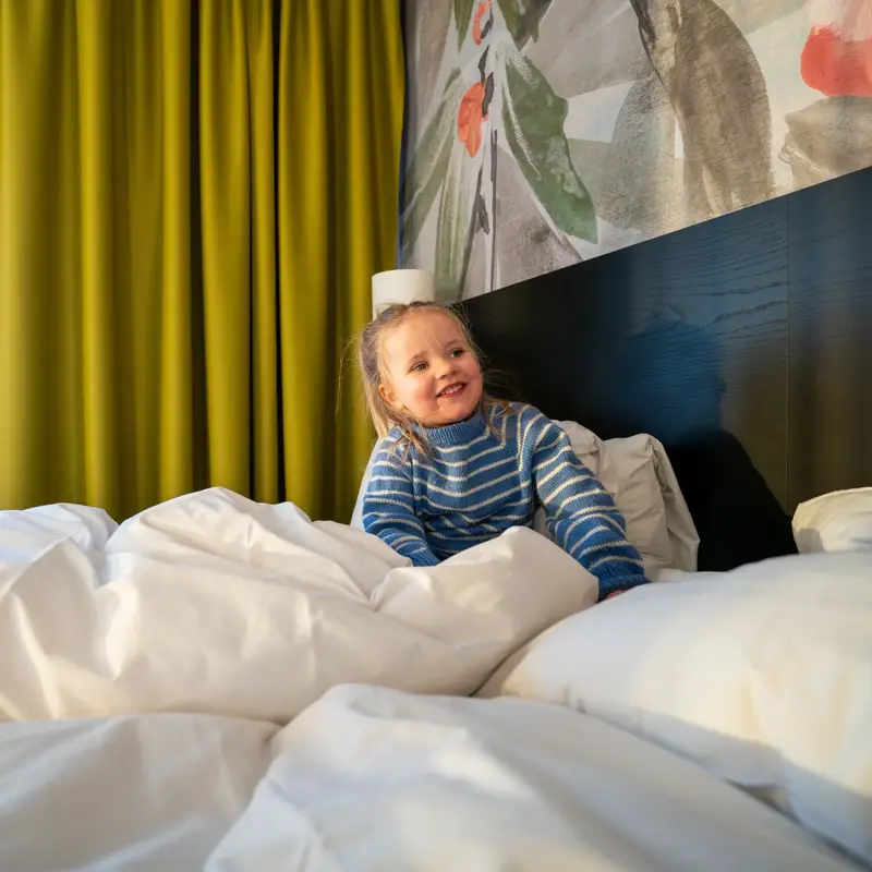Jente sitter i hotellseng.