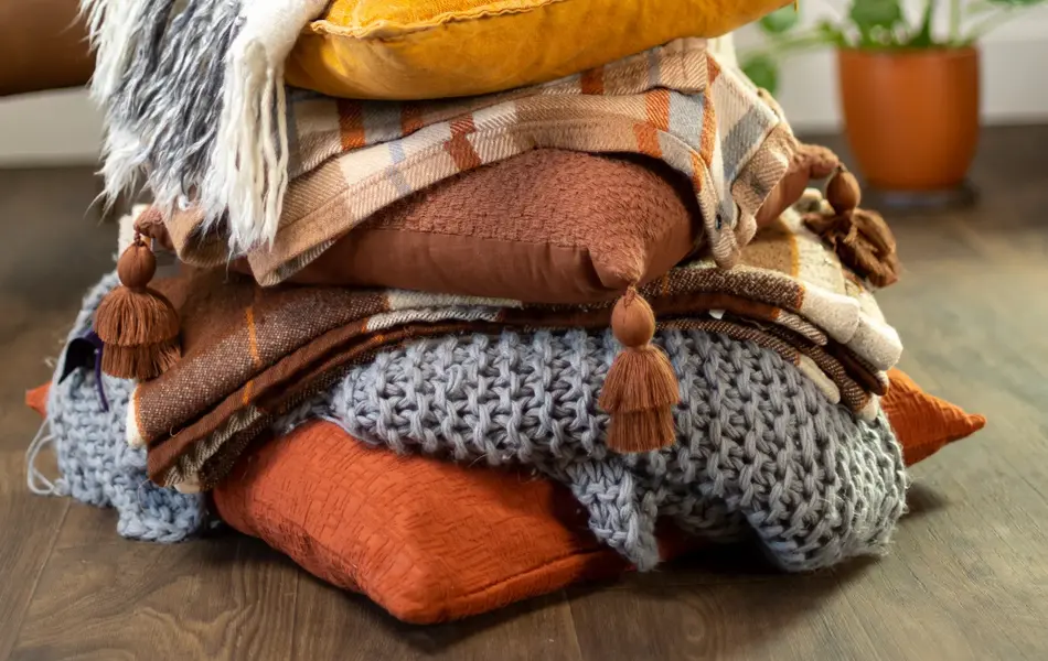 Nærbilde av stabel med puter og pledd med grønne planter i bakgrunnen 