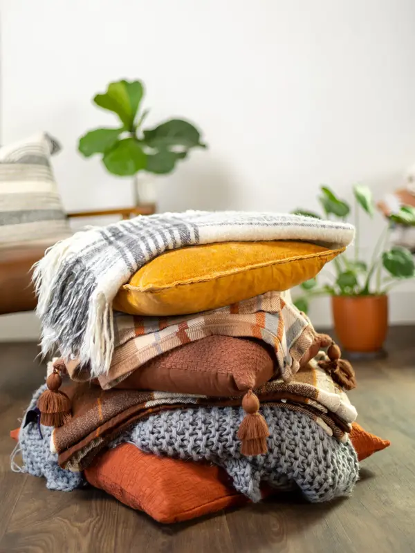 Nærbilde av stabel med puter og pledd med grønne planter i bakgrunnen 