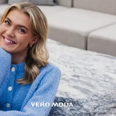 Blid-og-smilende-dame-med-lyst-langt-hår-og-lilla-strikkejakke-sittende-på-gulvet