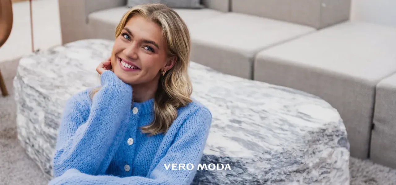 Blid-og-smilende-dame-med-lyst-langt-hår-og-lilla-strikkejakke-sittende-på-gulvet