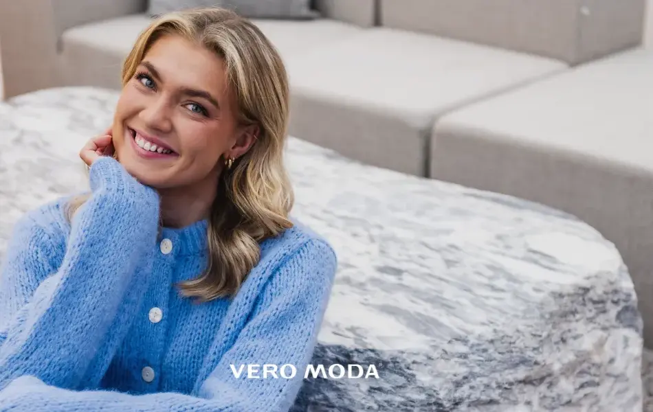 Blid-og-smilende-dame-med-lyst-langt-hår-og-lilla-strikkejakke-sittende-på-gulvet