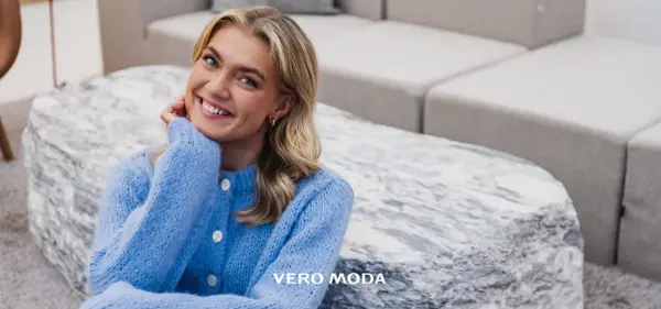 Blid-og-smilende-dame-med-lyst-langt-hår-og-lilla-strikkejakke-sittende-på-gulvet