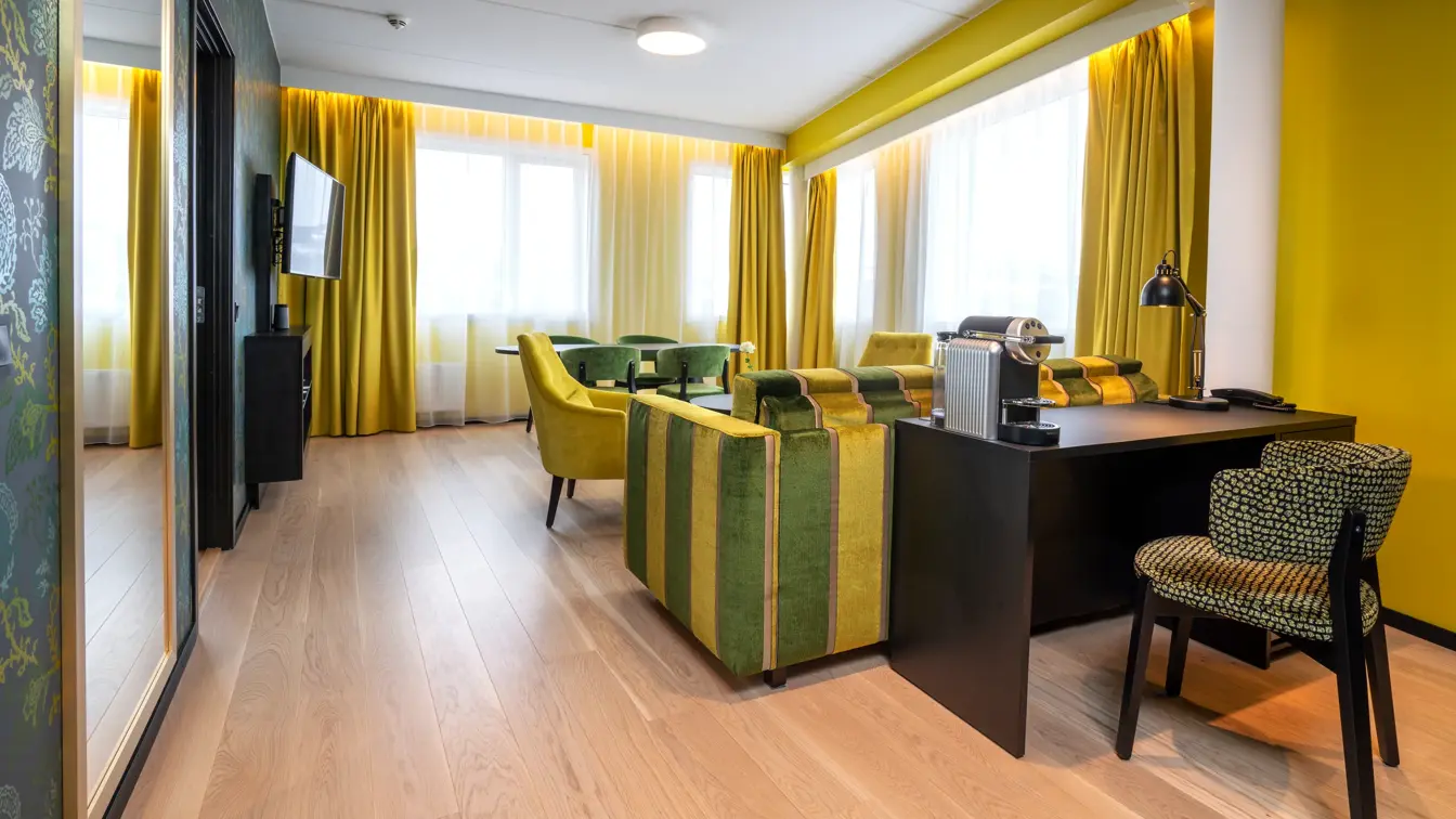 Stort speil, skrivebord med mønstrete stol, gule vegger og gul og grønn stripete sofa i suite på Thon Hotel Kirkenes