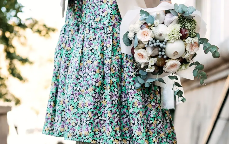 Halvportrett av dame i blomsterkjole og sneakers som holder en blomsterbukett