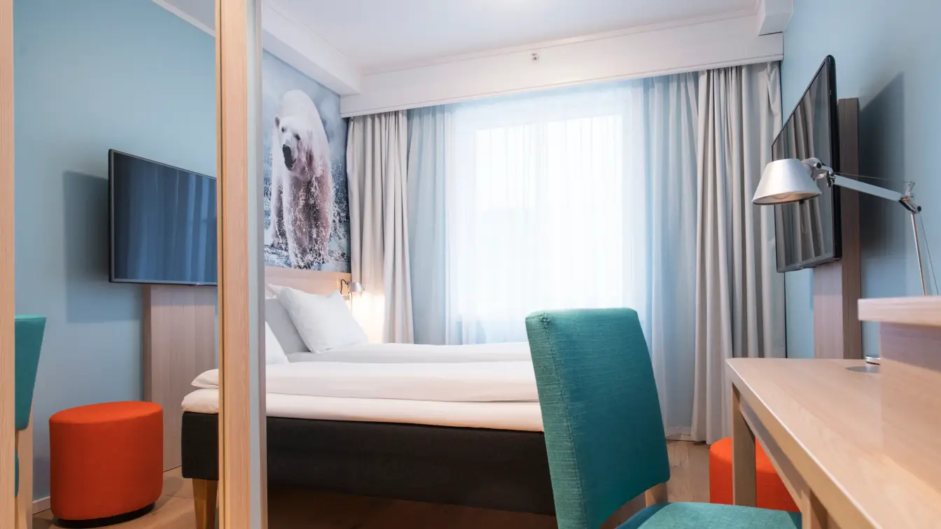 Sengen, kontorplass og tv på et dobbeltrom på Thon Hotel Polar, med et stort bilde av en isbjørn på veggen