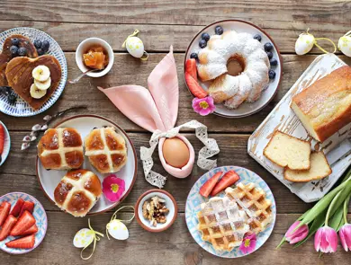 Easter festive dessert table with hot cross buns, cakes, waffles and pancakes. Overhead view
