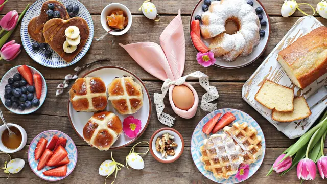 Easter festive dessert table with hot cross buns, cakes, waffles and pancakes. Overhead view