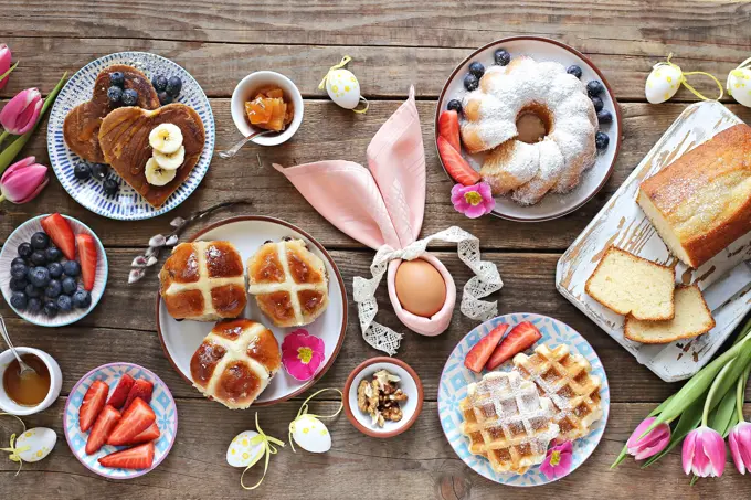 Easter festive dessert table with hot cross buns, cakes, waffles and pancakes. Overhead view