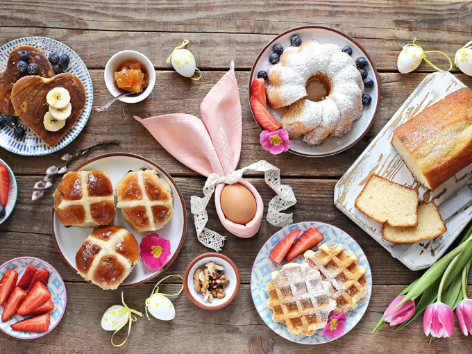 Easter festive dessert table with hot cross buns, cakes, waffles and pancakes. Overhead view