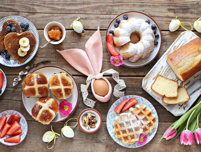 Easter festive dessert table with hot cross buns, cakes, waffles and pancakes. Overhead view