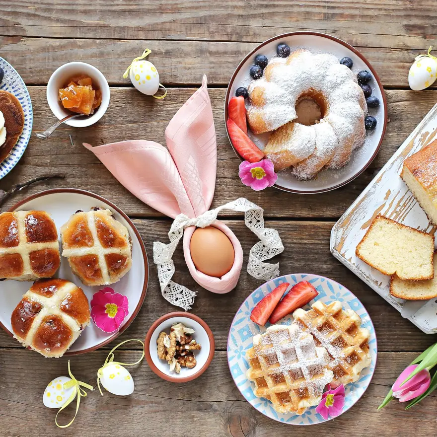 Easter festive dessert table with hot cross buns, cakes, waffles and pancakes. Overhead view