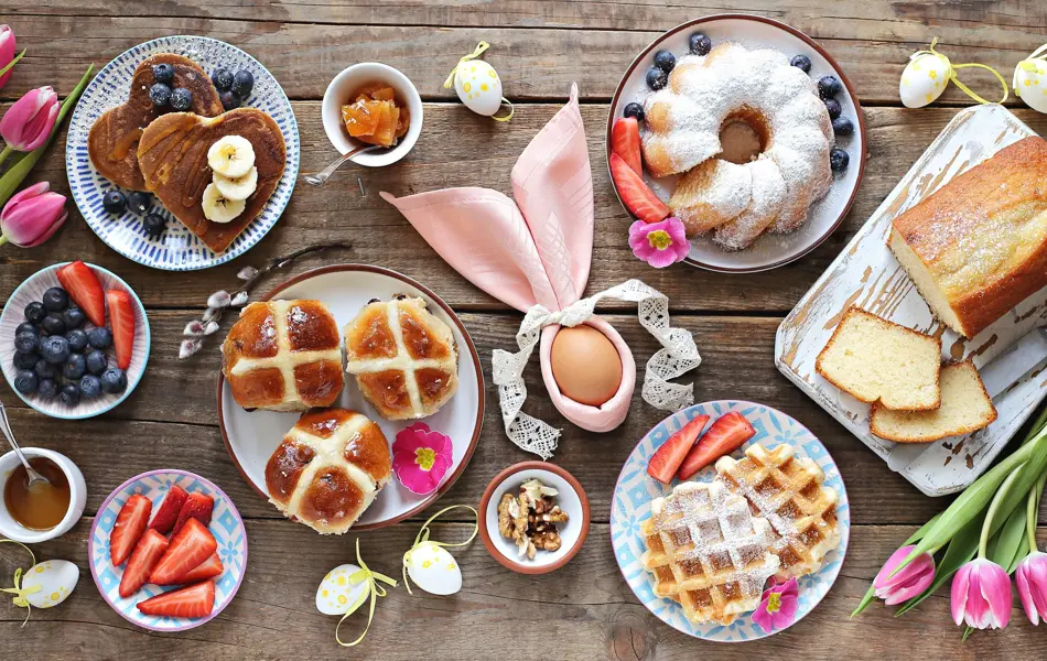 Easter festive dessert table with hot cross buns, cakes, waffles and pancakes. Overhead view