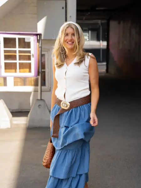 jente med hvitt hårtørkle, hvit topp, brunt belte, langt olaskjørt med kapper, brun veske