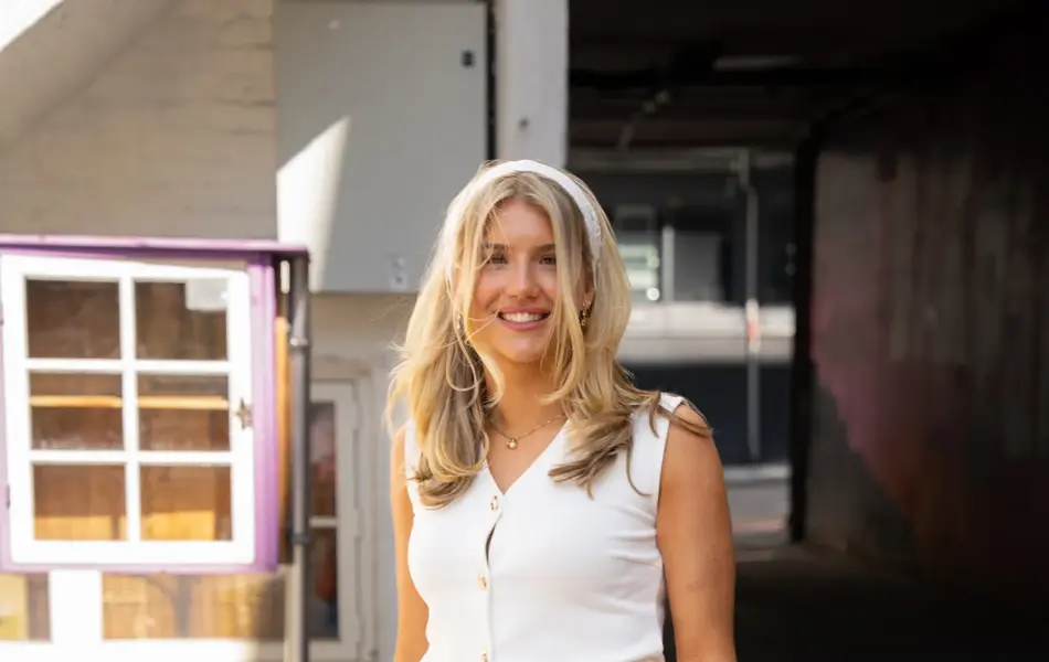 jente med hvitt hårtørkle, hvit topp, brunt belte, langt olaskjørt med kapper, brun veske