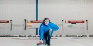 Mann som holder curling-stein på isen i en curlinghall. 