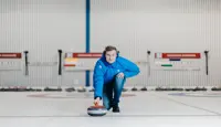 Mann som holder curling-stein på isen i en curlinghall. 