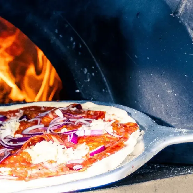 Pizza på vei inn i steinovn for steking.