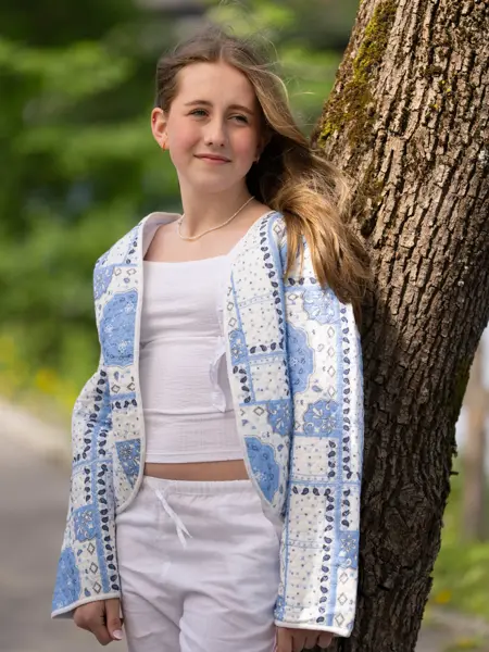 Jente står ute med hvit linbukse, hvit topp og blåmønstret jakke.