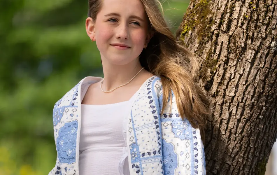 Jente står ute med hvit linbukse, hvit topp og blåmønstret jakke.