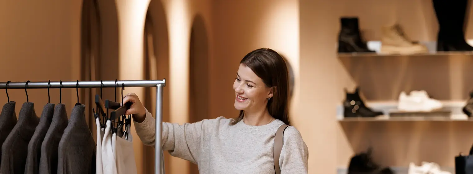 En kvinne står i en klesbutikk og ser på klær som henger på et stativ