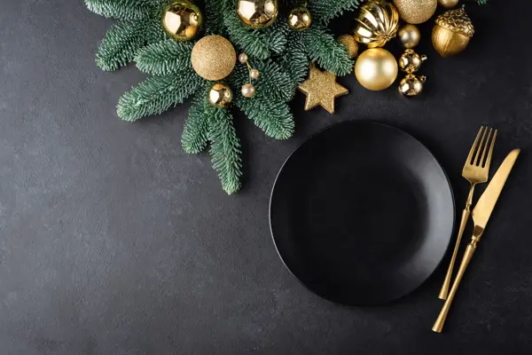 Christmas or New Year table setting background with black plate and golden color cutlery. Top view with copy space for text, design elements, graphics