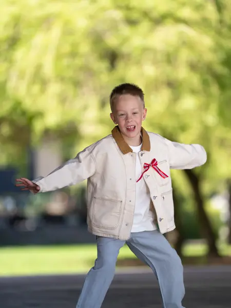 Liten gutt i lys jakke, hvit t-skjorte, blå bukse og beige tøysko