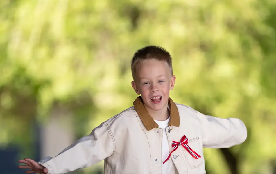 Liten gutt i lys jakke, hvit t-skjorte, blå bukse og beige tøysko