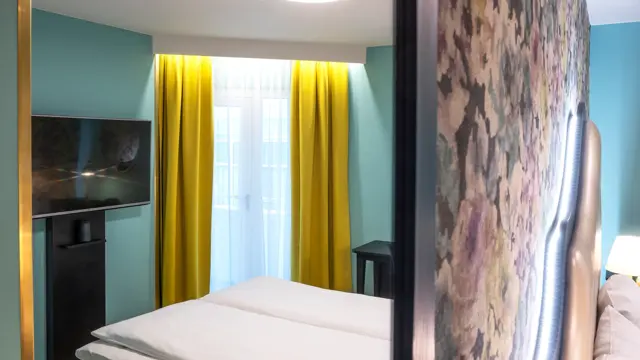 Blomstret tapet og dobbeltseng i dobbeltrom med speilbilde av resten av rommet, som har gule gardiner og tv på Thon Hotel Cecil i Oslo sentrum