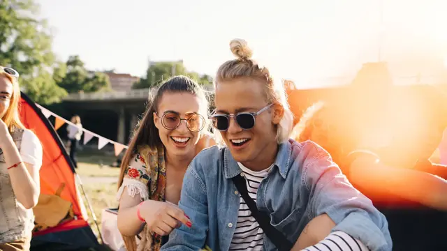 En ung mann og en dame sitter på bakken. Begge smiler.