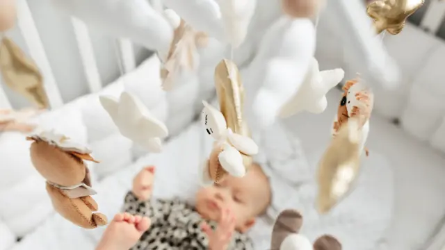 Little baby girl sleeps on a bed in a green suit, playmobile revolves over her.