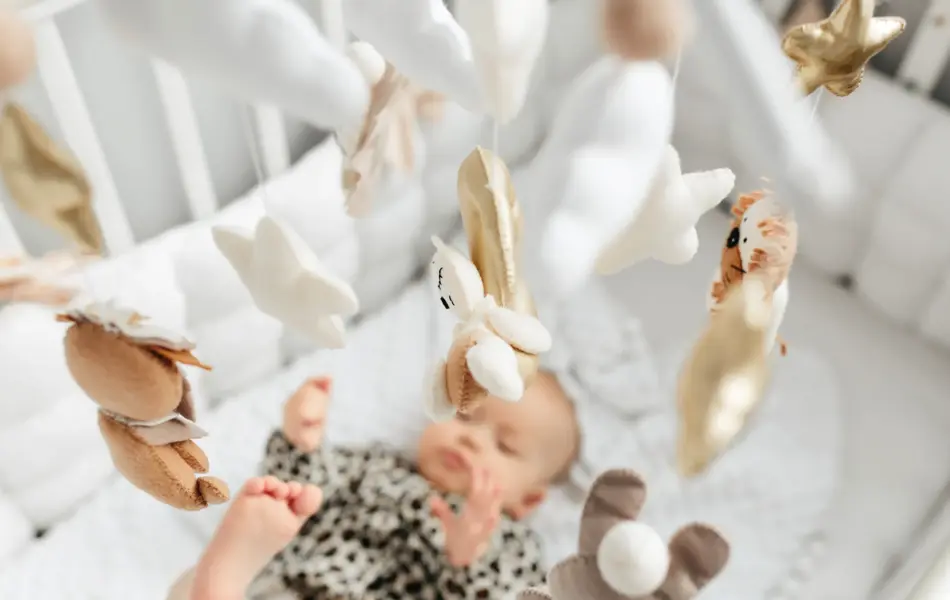 Little baby girl sleeps on a bed in a green suit, playmobile revolves over her.