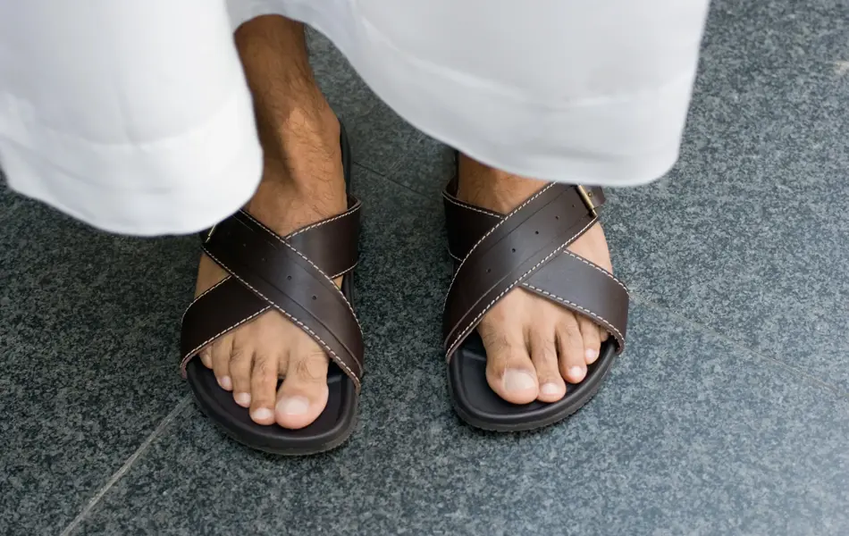 Nærbilde av manneføtter med brune skinnsandaler og hvit bukse 