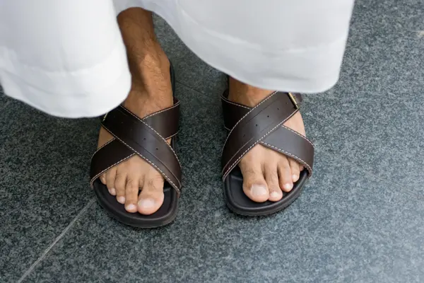 Nærbilde av manneføtter med brune skinnsandaler og hvit bukse 