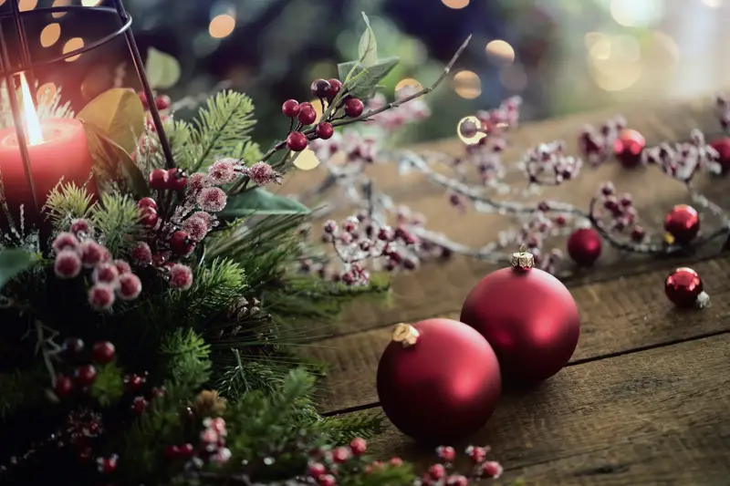 Christmas lantern and holiday baubles in red, festive and sparkling lights on a wood surface.